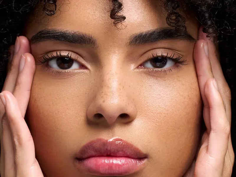 Gros plan d’un regard aux sourcils denses et structurés, mains posées de part et d’autre du visage